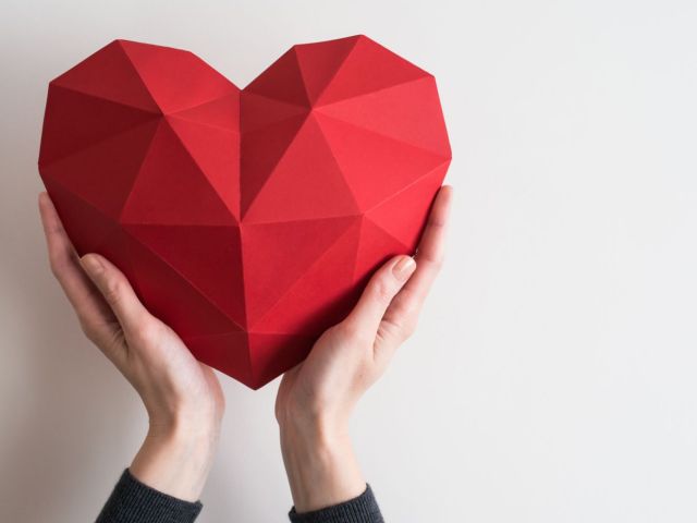 Female hands holding red polygonal paper heart shape