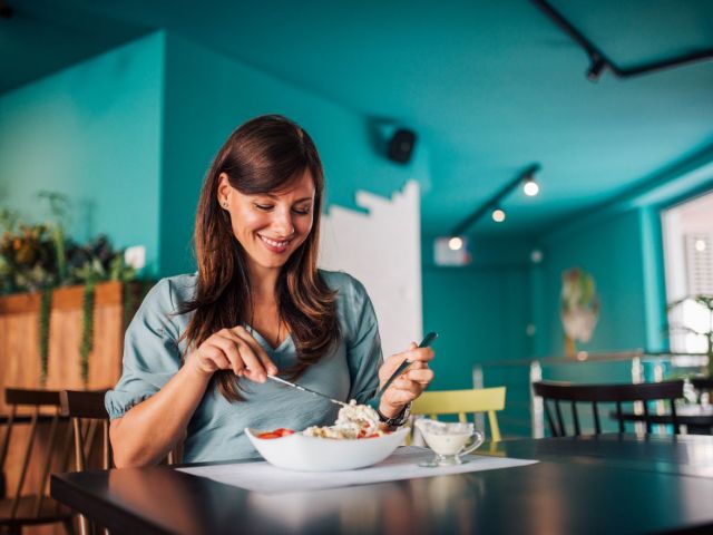 Positive woman eating salad at cozy cafe.